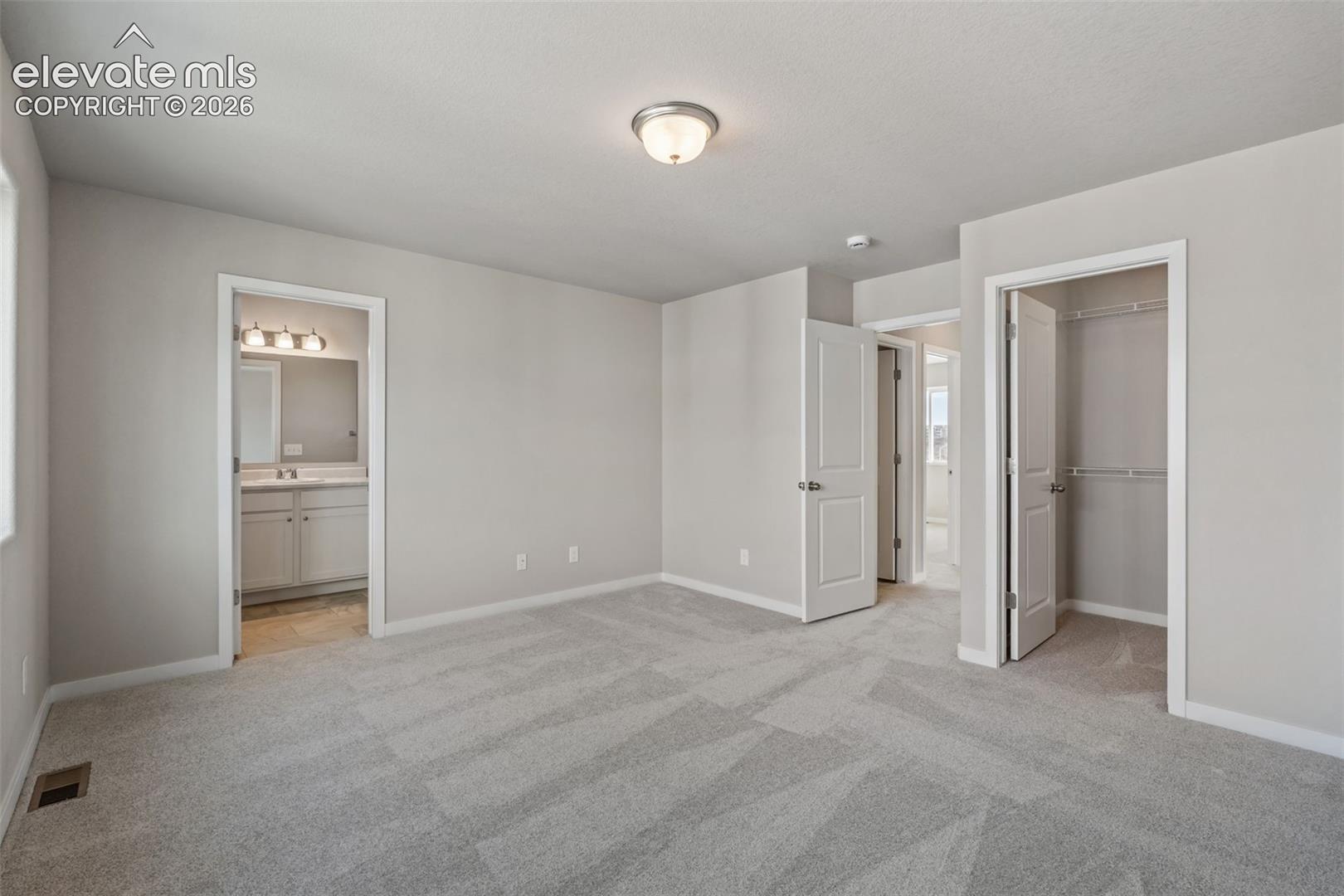 bedroom with neutral walls, ceiling light, doorway to bathroom with vanity lights, and an open closet — virtually staged