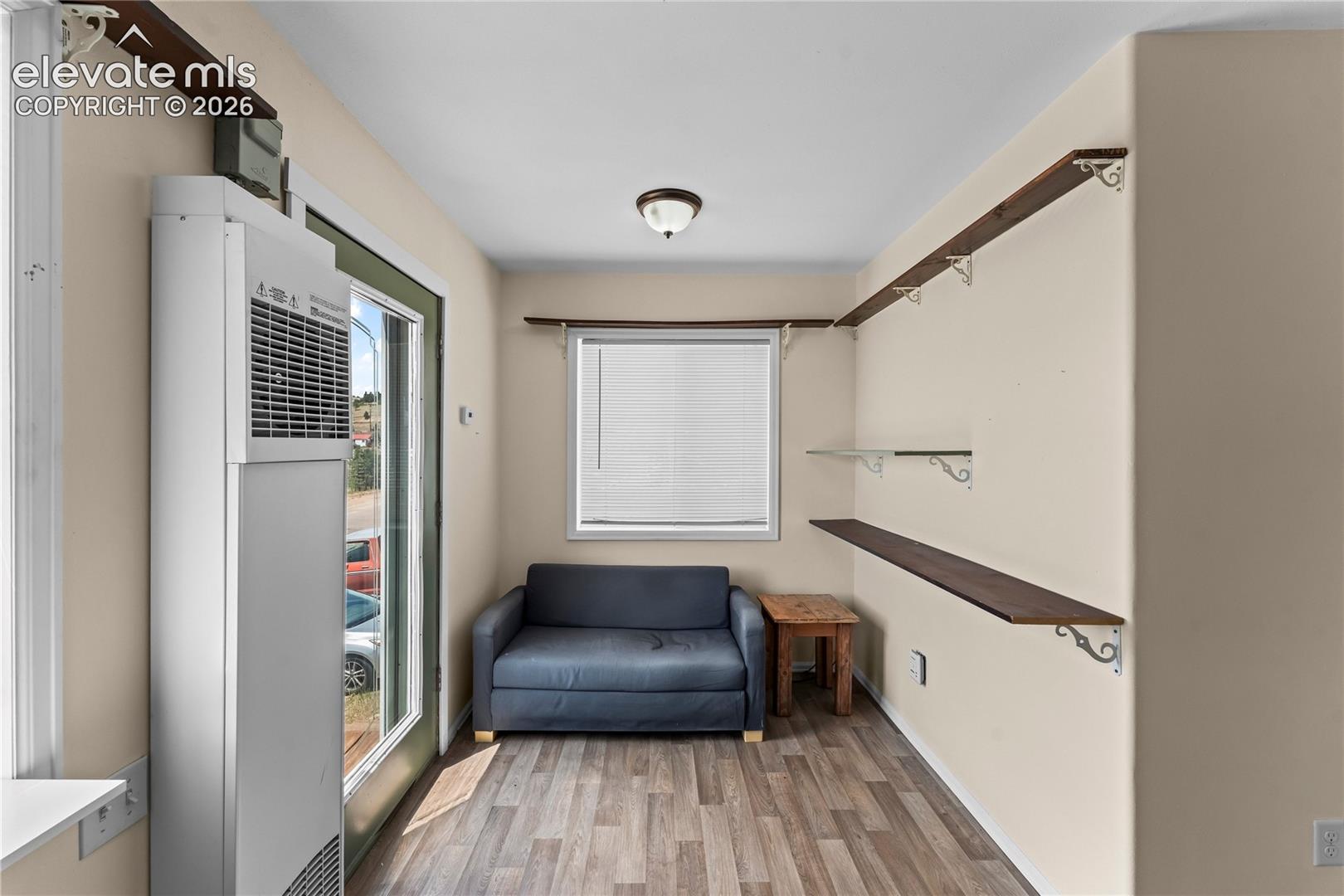 Open concept room featuring wood-finish flooring, a wall-mounted heating unit, and an exterior glass-paneled door