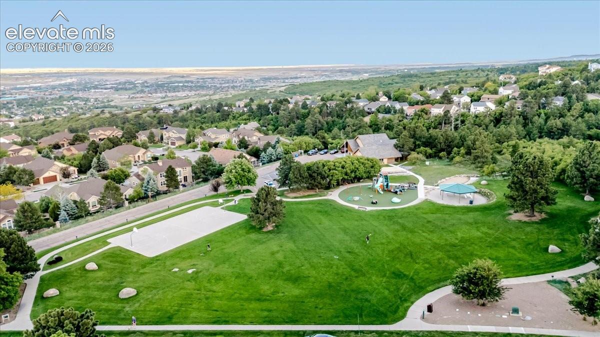 Expansive community park featuring a large green space, paved walking paths, children's play areas with covered structures, a sand volleyball court, and mature trees