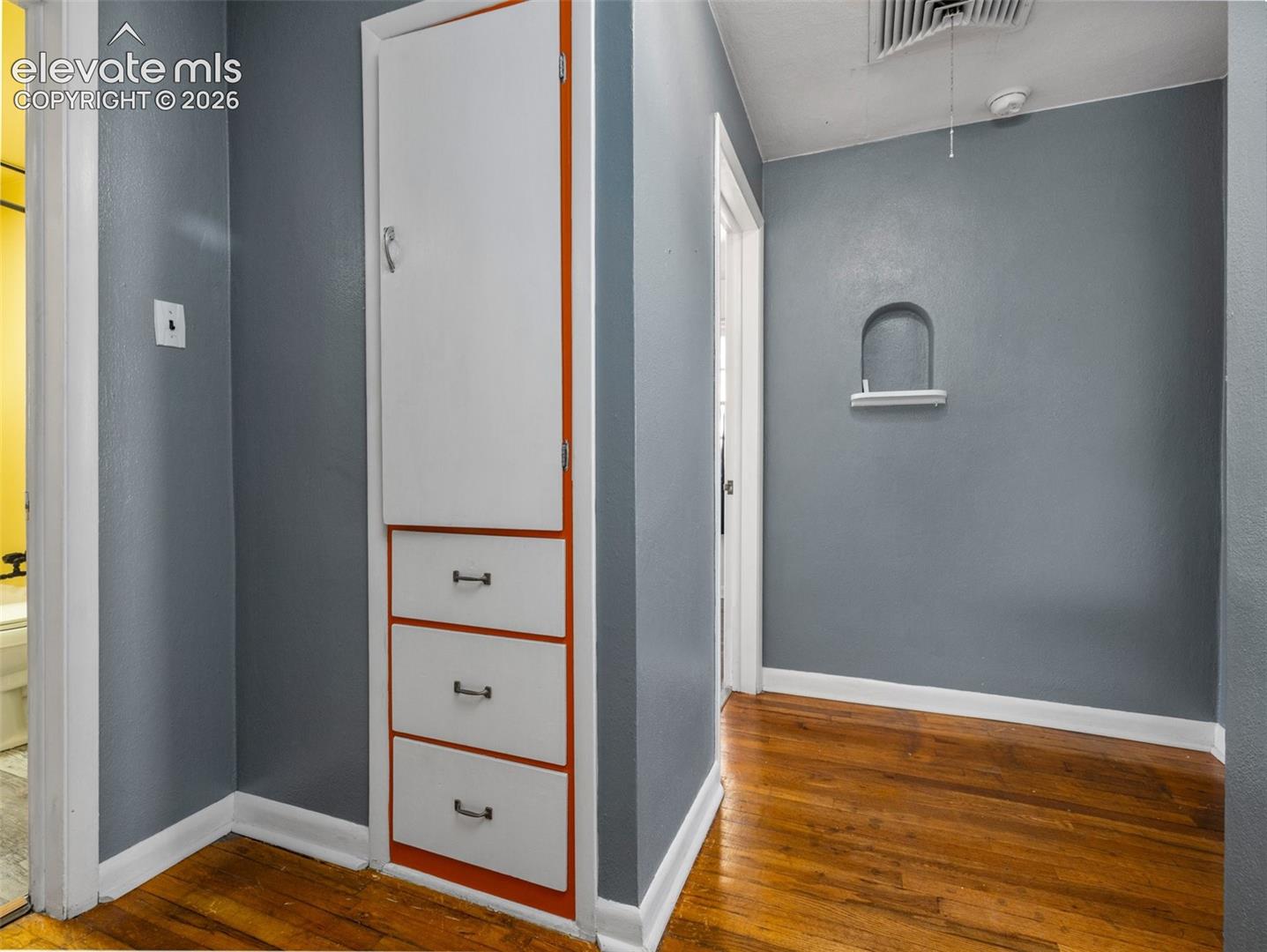 Built-in cabinetry featuring white doors and drawers with dark hardware, hardwood flooring, and a decorative arched wall niche with a display shelf