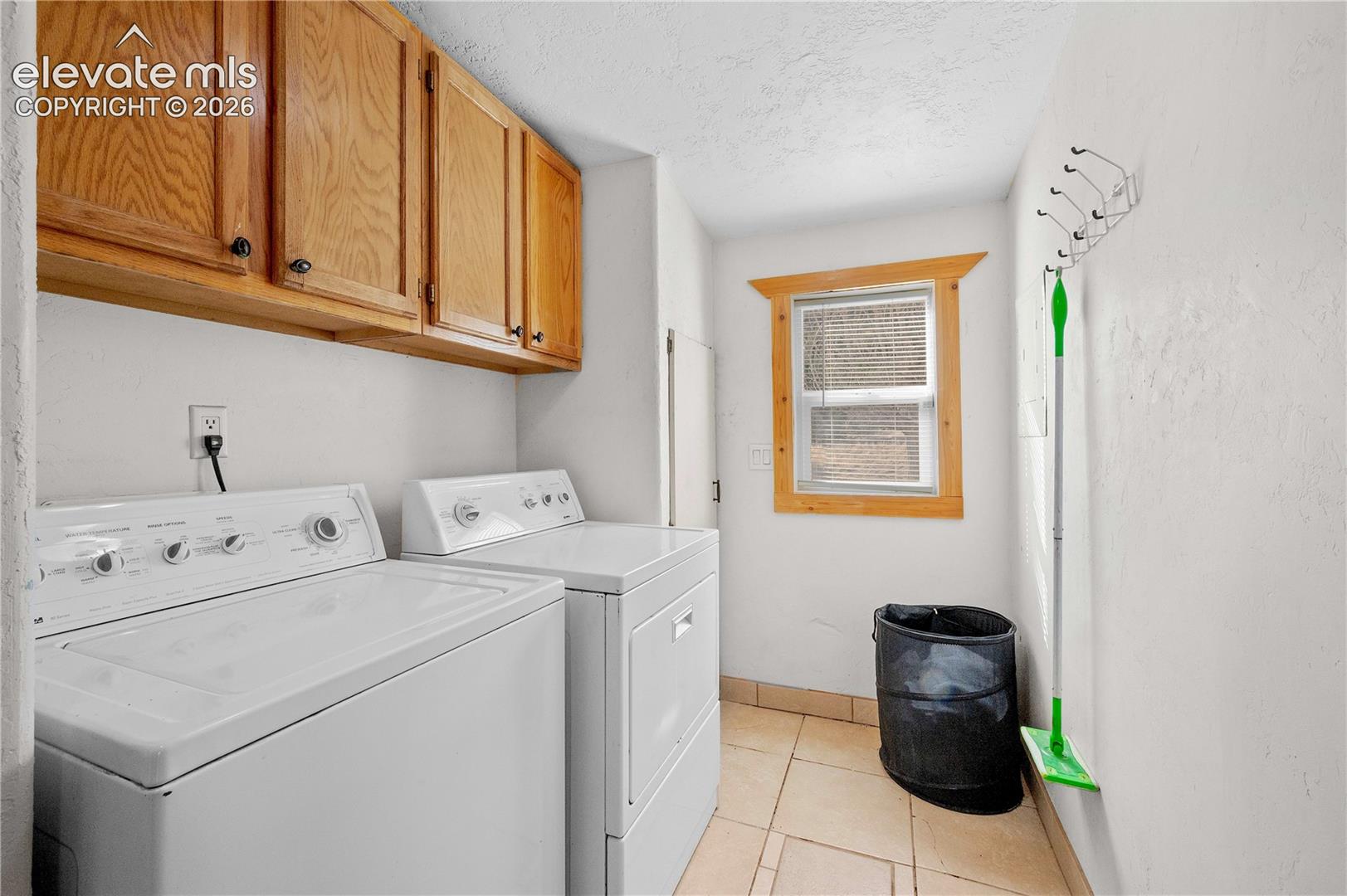 Clothes washing area featuring cabinets, a textured ceiling, light tile patterned flooring, and washing machine and dryer