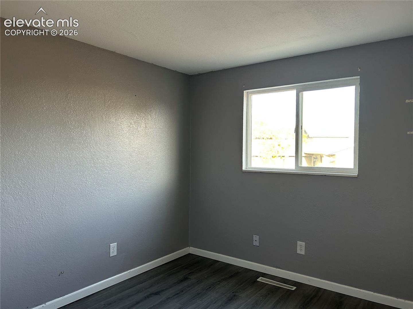 Interior room featuring neutral gray wall paint, a white-framed sliding window, and wood-finish flooring