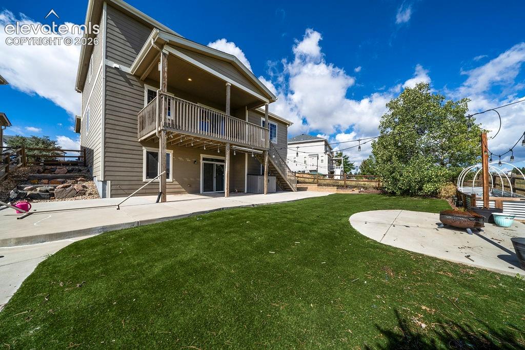 Expansive backyard featuring a manicured lawn, concrete patio, a second-story deck, and sliding glass doors