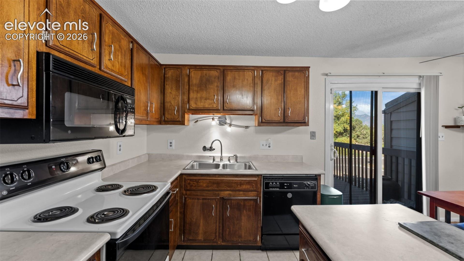 Kitchen featuring wood cabinetry, integrated microwave, black finish appliances, dual-basin sink with gooseneck faucet, and glass sliding door access to exterior space