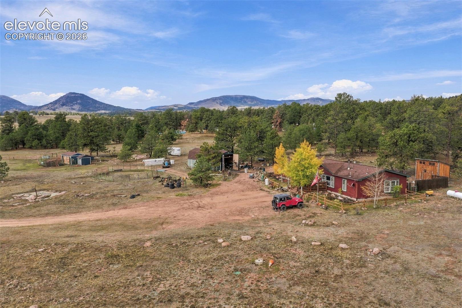 Rural acreage featuring a single-story residence, multiple outbuildings, mature evergreen trees, and a mountain backdrop