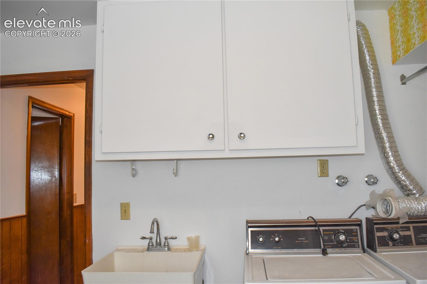 White upper cabinetry, utility sink with chrome faucet, power outlets, and wall-mounted hooks