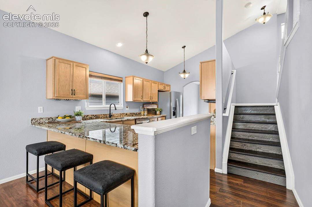 Kitchen featuring stone countertops, cabinetry with a natural wood finish, a peninsula with bar seating, pendant lighting, and wood-finish flooring