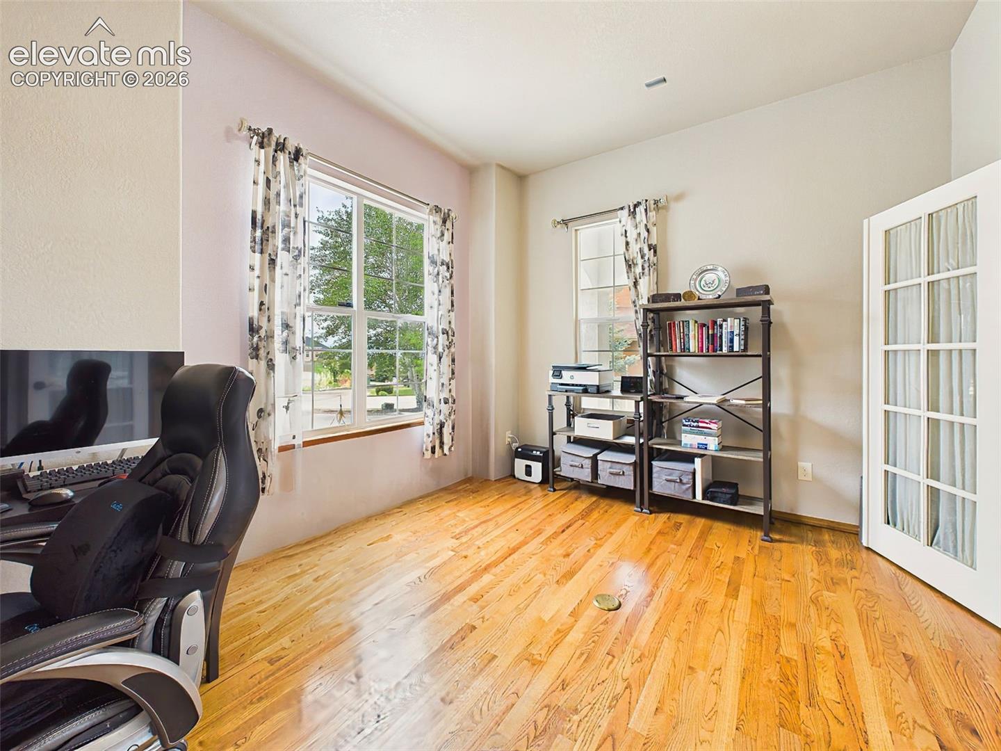 Bright main-level office featuring large windows, hardwood floors, and French door entry for added character.
