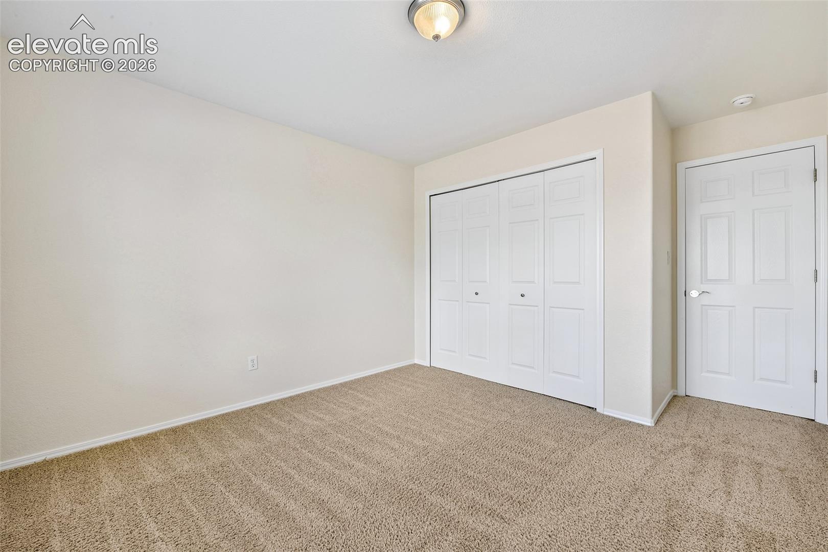 Textured carpeting, neutral wall paint, white bi-fold closet doors, and a paneled white door with chrome hardware
