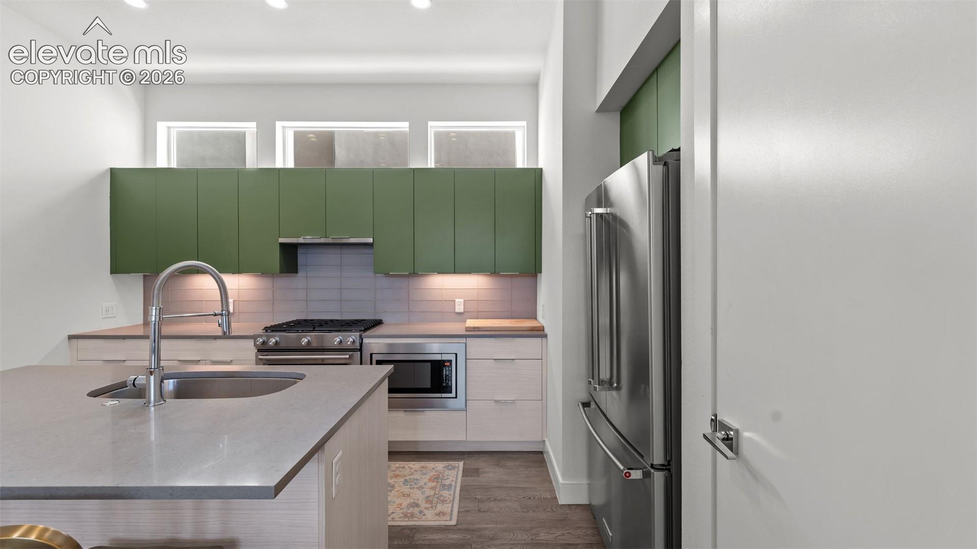 Kitchen featuring matte green cabinetry, quartz countertops, a stainless steel appliance suite, stacked tile backsplash, and transom windows