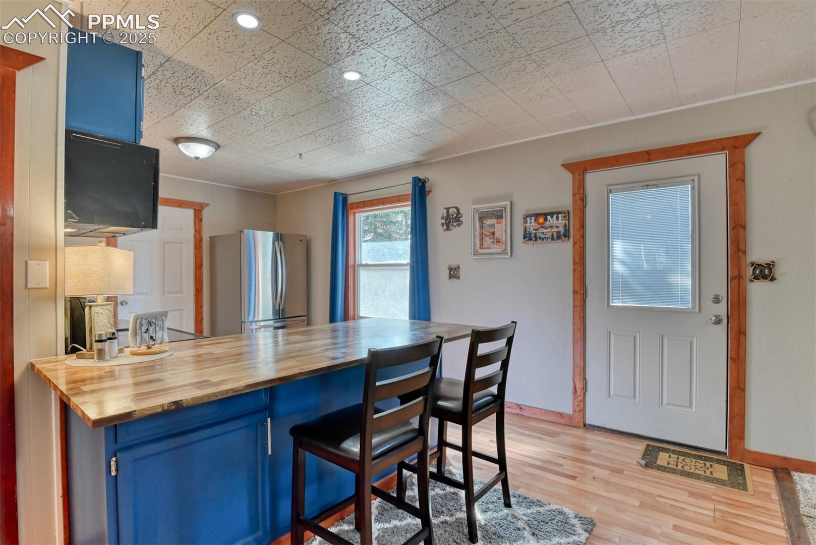 Kitchen with blue cabinets, wood counters, a breakfast bar area, light wood-style flooring, and freestanding refrigerator
