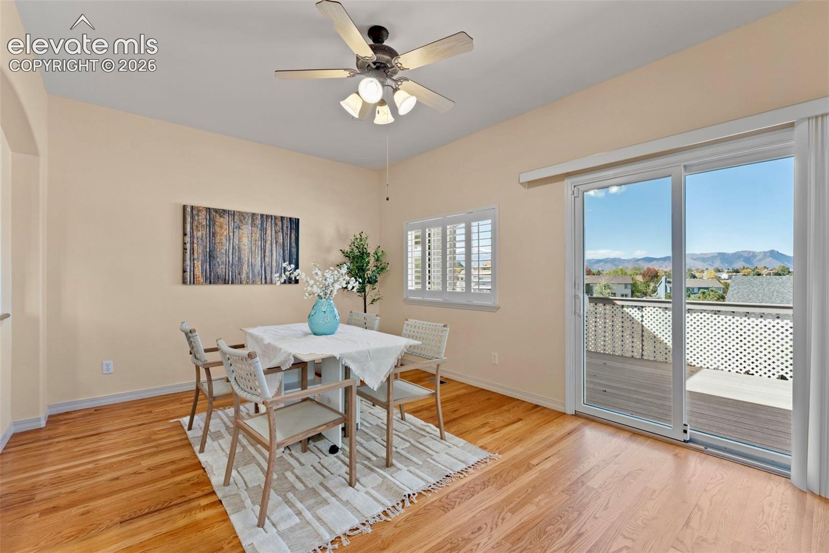 Wood-finish flooring, sliding glass door, white plantation shutters, ceiling fan with integrated lighting, and mountain backdrop