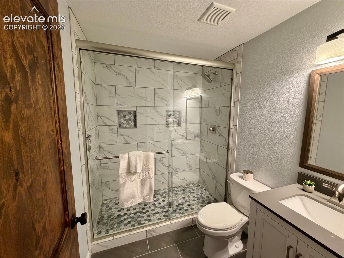 Basement Bathroom-Contemporary bathroom featuring a walk-in shower with glass enclosure, white marble-look subway tile, and hexagonal floor tile