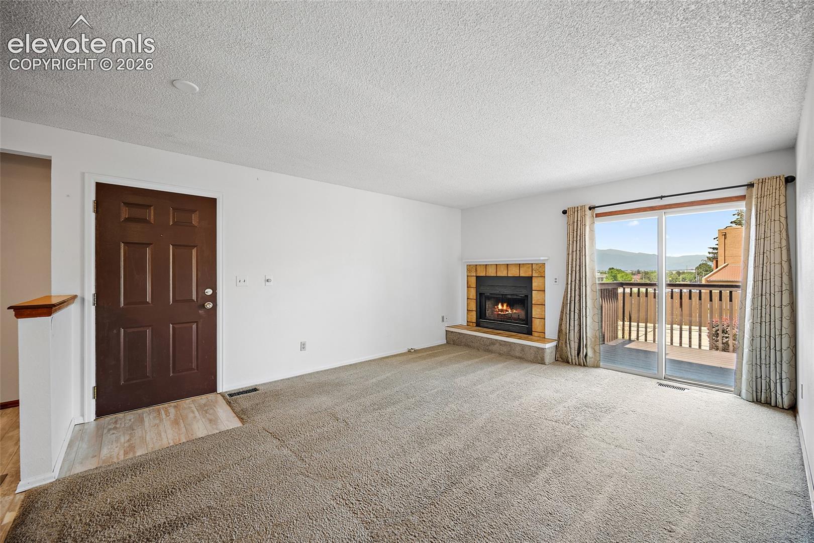 Spacious living area featuring a fireplace with a tile surround, carpeted flooring, and glass sliding doors opening to an outdoor balcony