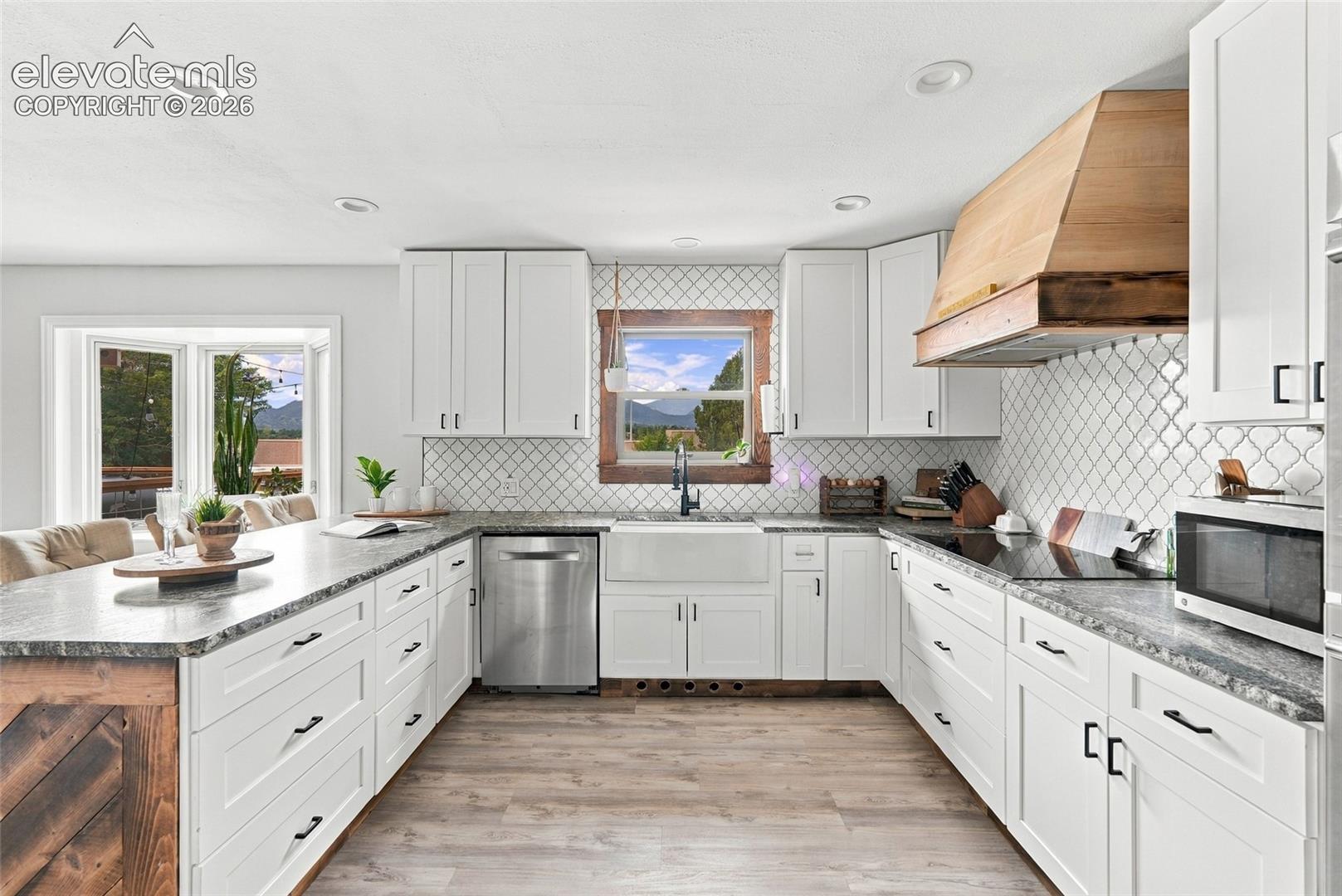 White shaker cabinetry with black hardware, wood-finish flooring, stone countertops, stainless steel appliances, and a tile backsplash