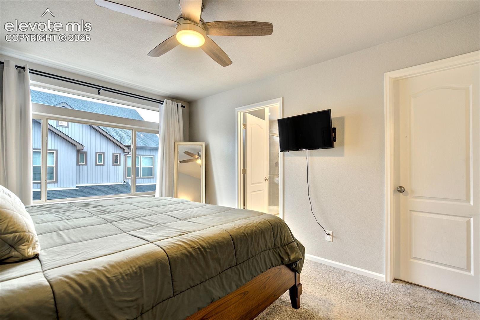 Expansive window with horizontal panes, overhead ceiling fan with light fixture, neutral carpeted flooring, and two-panel interior doors
