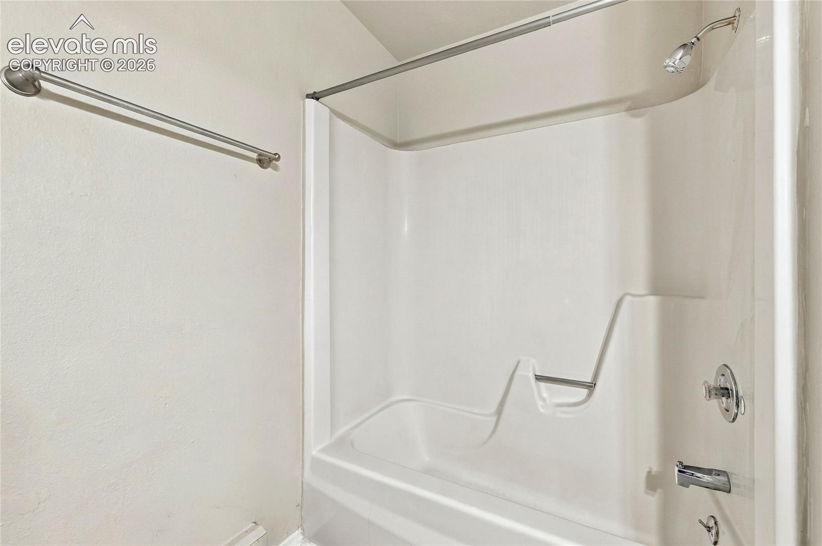 Bathtub and shower combination with a molded surround, chrome finish plumbing fixtures, and a wall-mounted metal towel bar