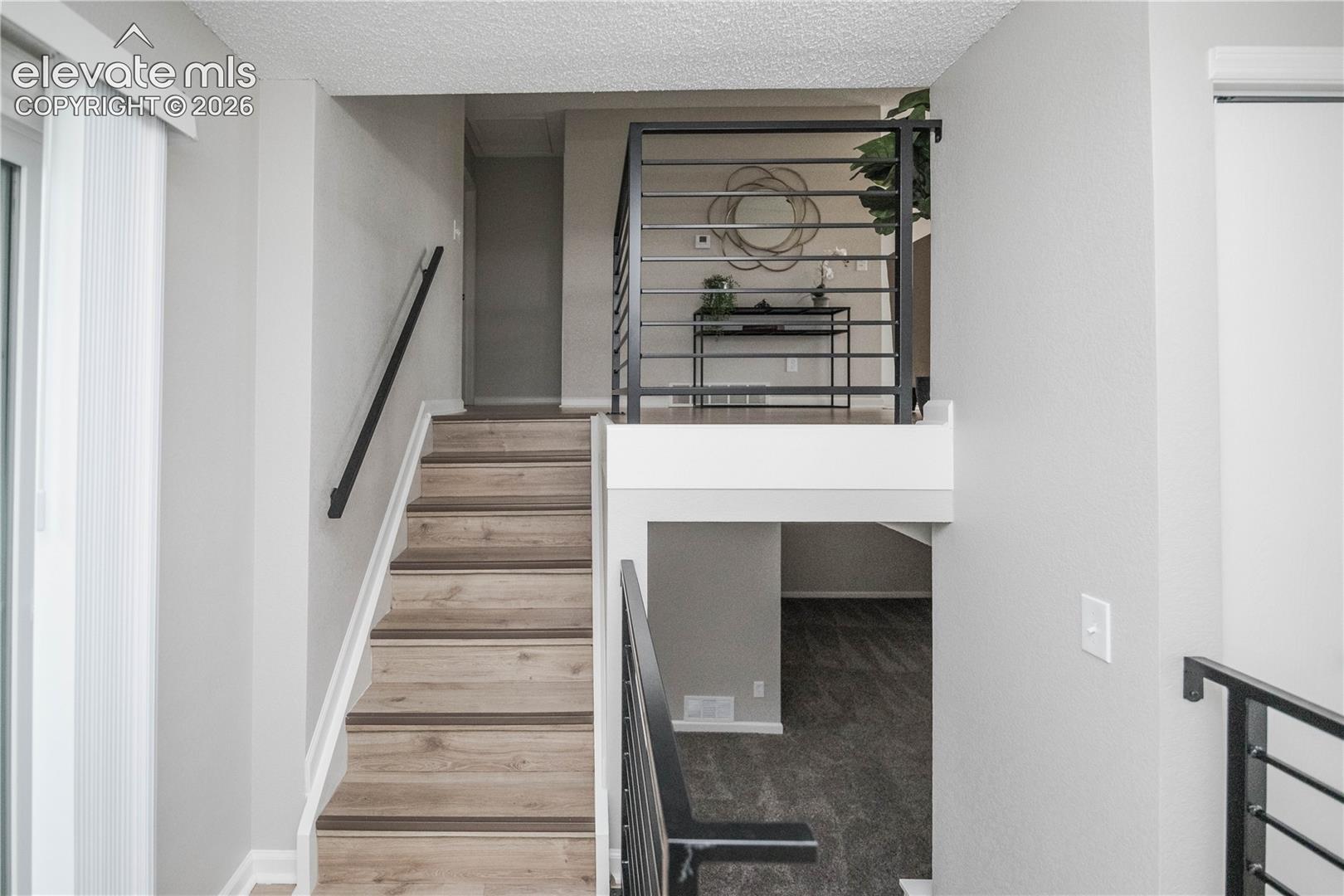 Staircase featuring wood-finish treads, matte black handrails, and industrial-style metal horizontal railing