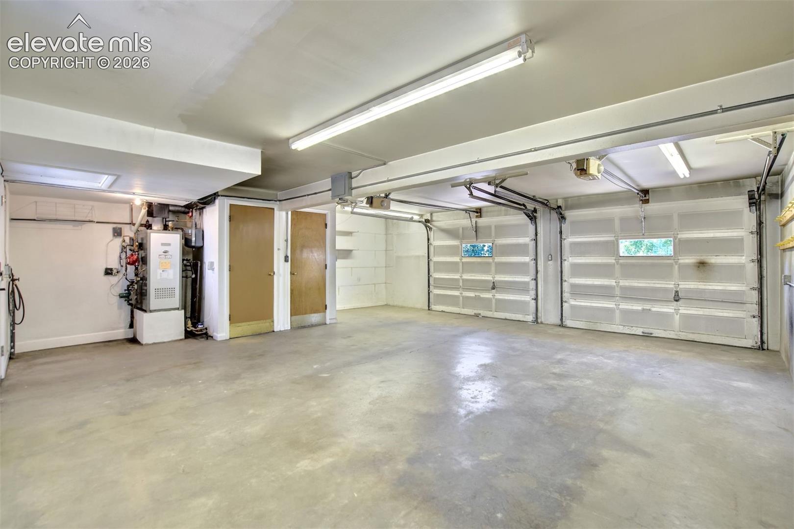 Two-car garage featuring concrete flooring, fluorescent overhead lighting, dual paneled metal garage doors, and built-in utility storage