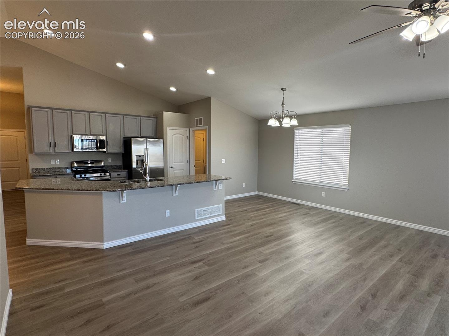 Vaulted ceilings, wood-finish flooring, kitchen peninsula with stone-finish countertops, recessed lighting, and a multi-light chandelier