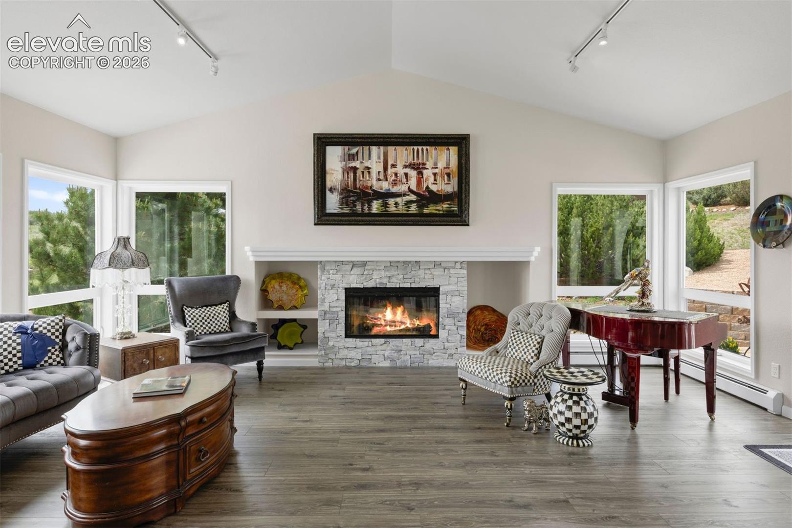 Great room with stacked stone gas fireplace, built-in shelving, vaulted ceiling, and large windows on all sides.