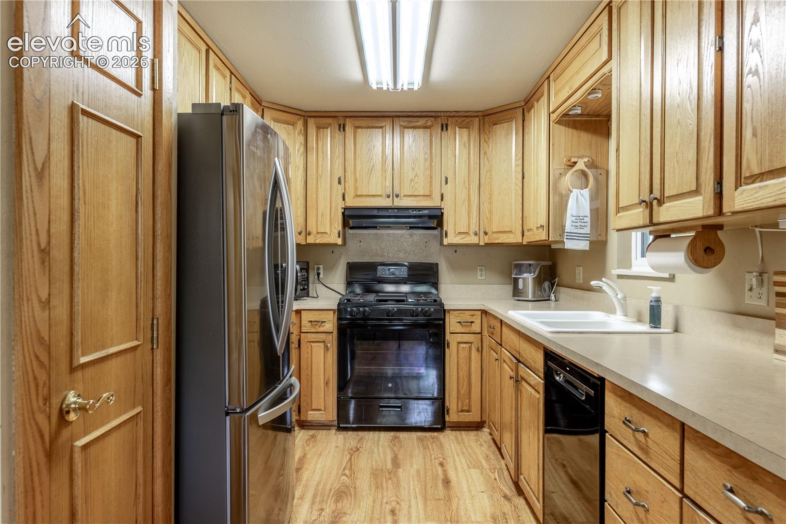 Kitchen featuring natural wood cabinetry, stainless steel French door refrigerator, black range, integrated dual-basin sink, and wood-finish flooring