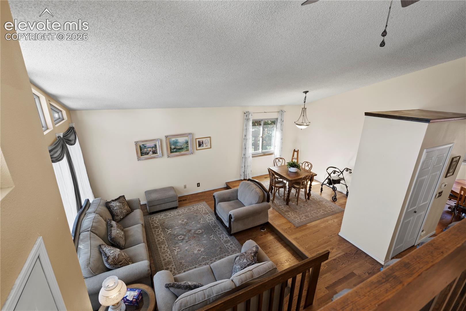 Vaulted ceiling with textured finish, wood-finish flooring, and multiple window placements providing natural illumination