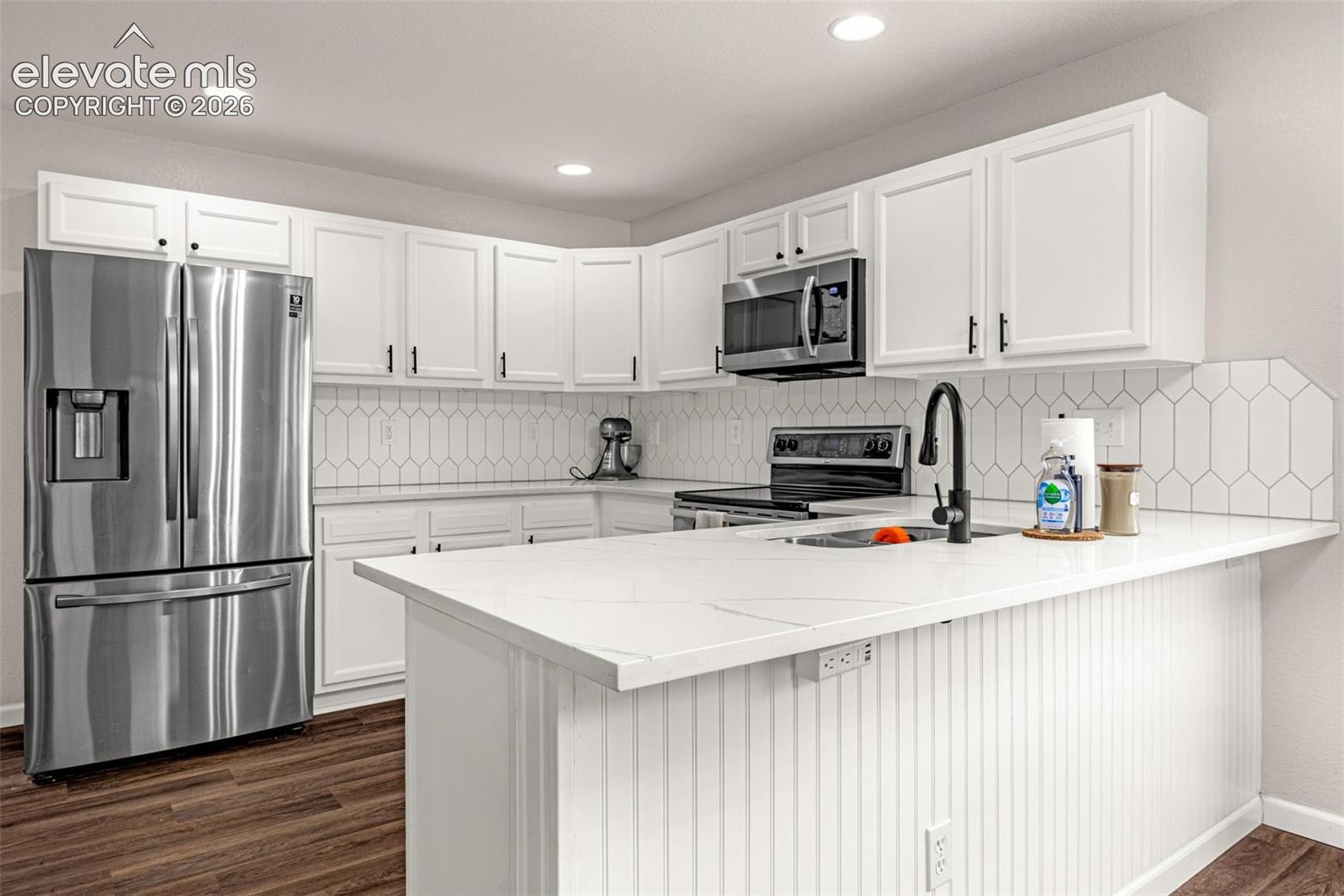Kitchen featuring white cabinetry, solid-surface countertops, a geometric-pattern tile backsplash, stainless steel appliances, and wood-finish flooring
