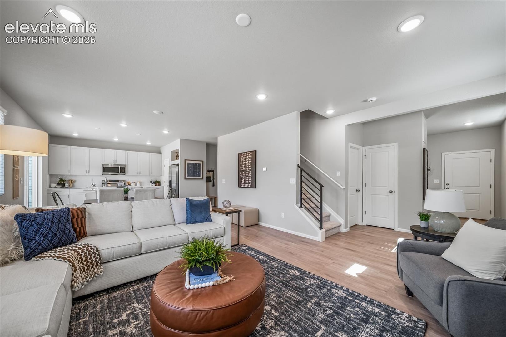Open-concept living area with wood-finish flooring, recessed lighting, and a staircase with a black metal railing
*photos of a model home*