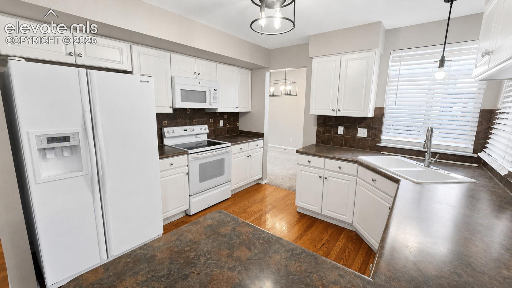 White paneled cabinetry, wood-finish flooring, undermount sink, and recessed lighting