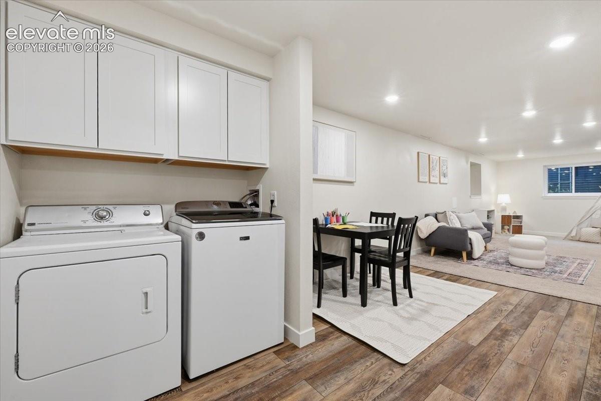 Wood-finish flooring throughout, white upper cabinetry, recessed ceiling lighting, and a full-size washer and dryer