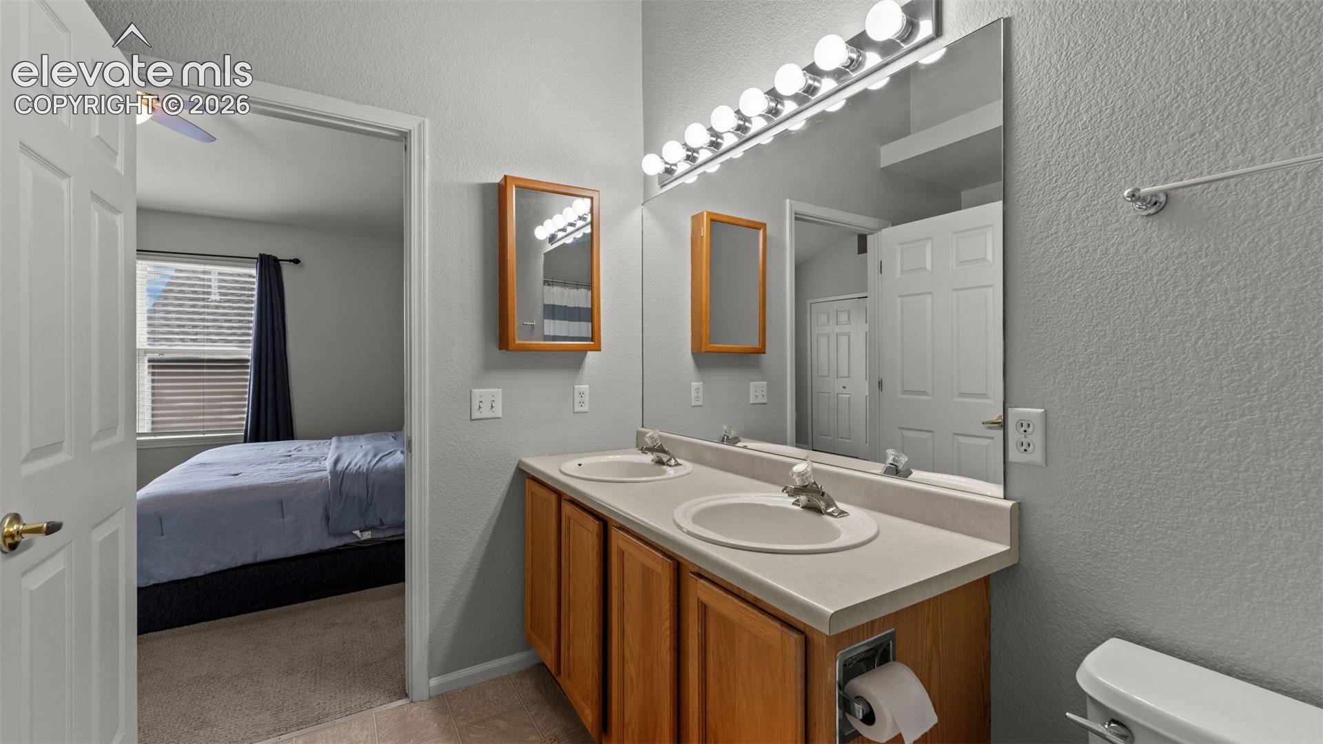 Dual-sink vanity with a solid-surface countertop, wood-finish cabinetry, wall-mounted medicine cabinet, and expansive wall-to-wall mirror with multi-bulb lighting fixture