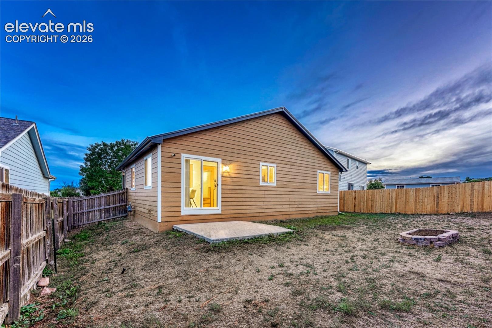 Large fenced backyard with sprinkler system, patio, and raised flower bed.