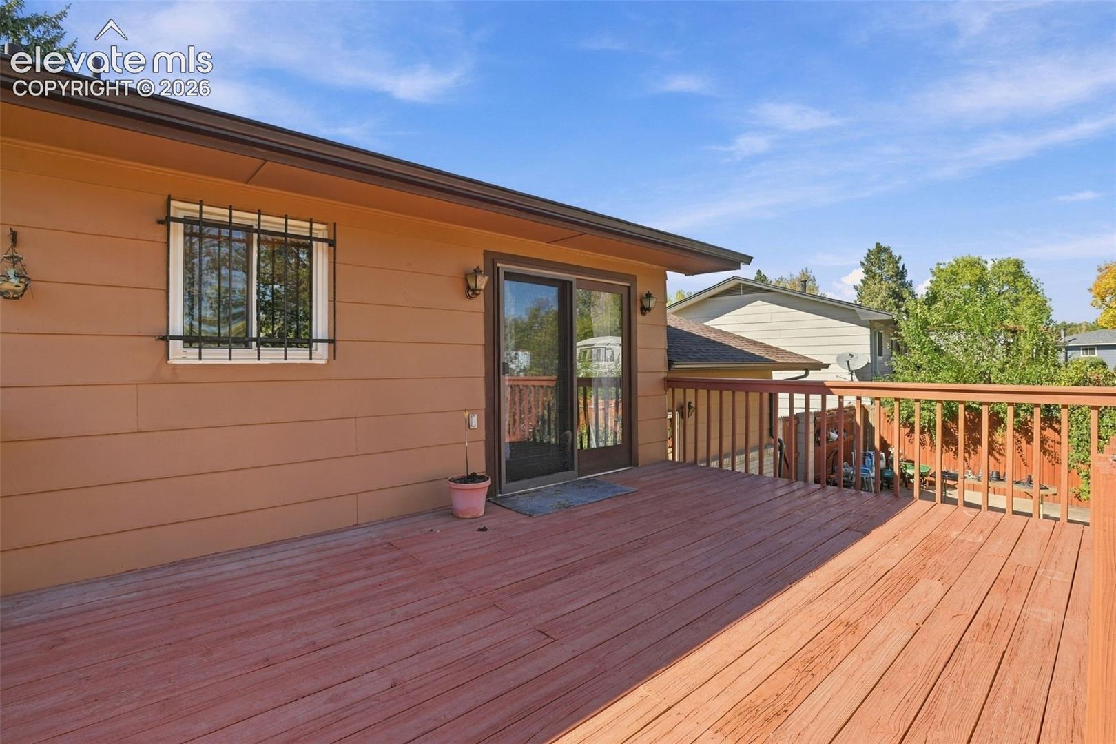 Elevated wood deck featuring vertical baluster railings, horizontal siding, sliding glass door, and exterior wall-mounted lighting