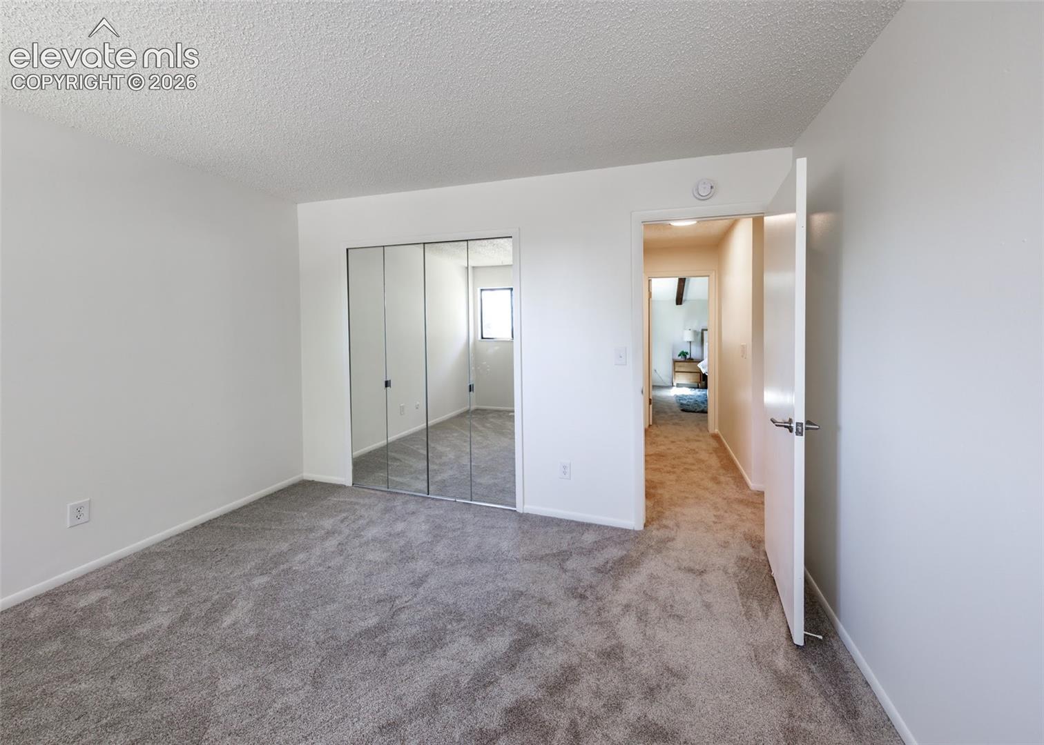 Bedroom featuring neutral-toned carpeting, mirrored sliding closet doors, and textured ceiling finish