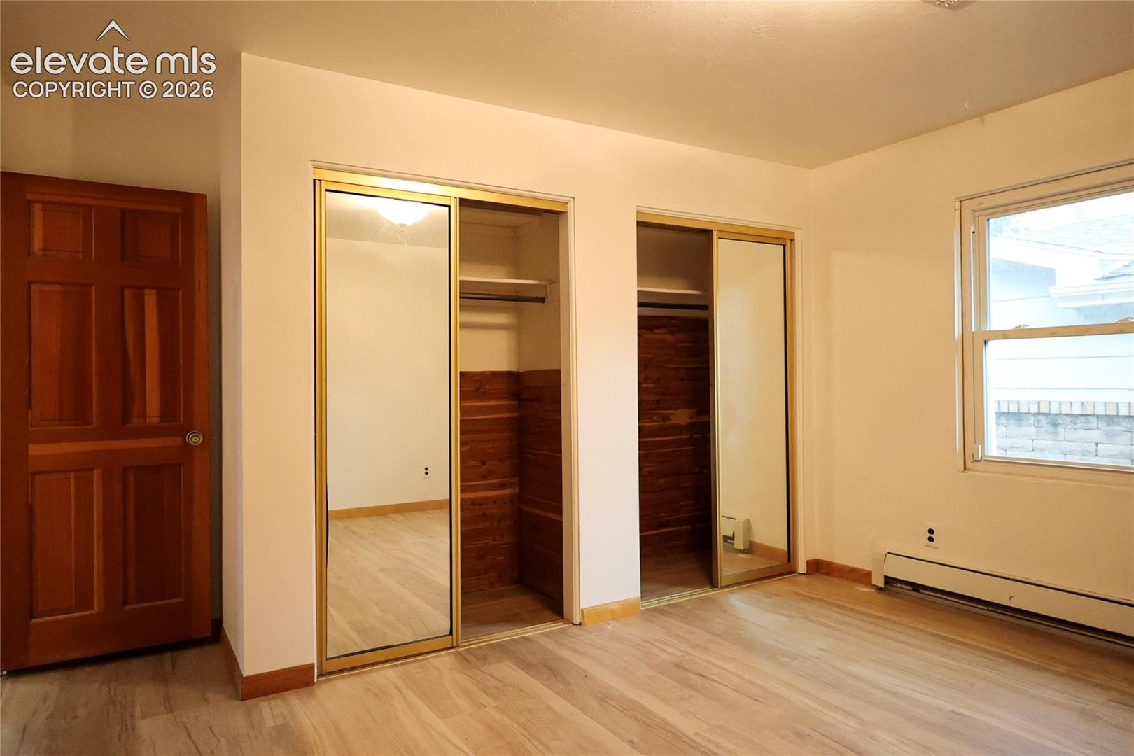 Bedroom 3 Wood-finish flooring, two closets with mirrored sliding doors, and a window with a white frame