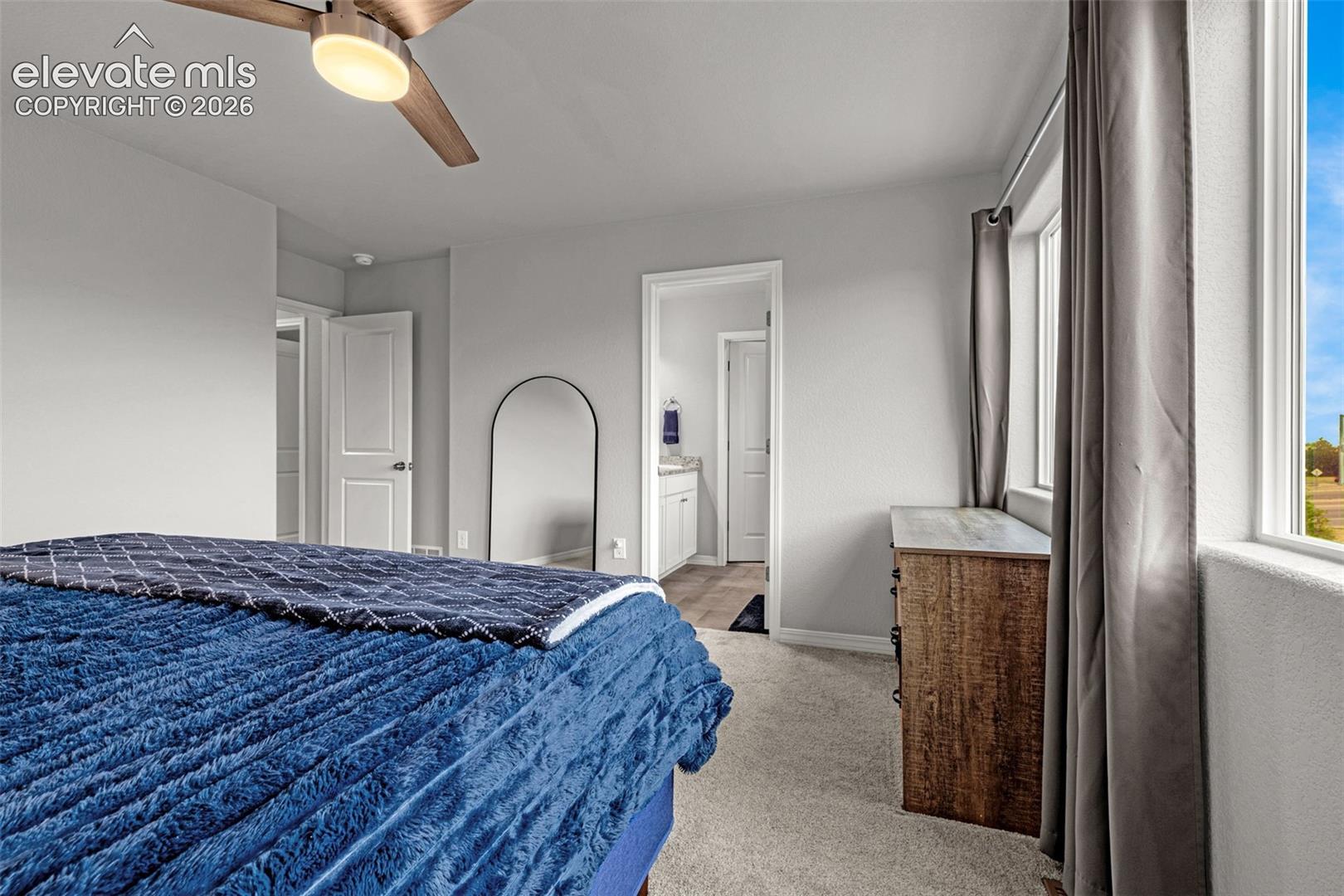 Spacious bedroom featuring light gray walls, plush carpet flooring, and a modern ceiling fan with integrated lighting