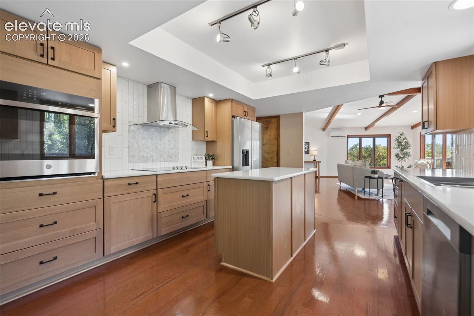 Light wood-finish cabinetry, stainless steel appliances, white countertops, a tiled backsplash, and recessed and track lighting