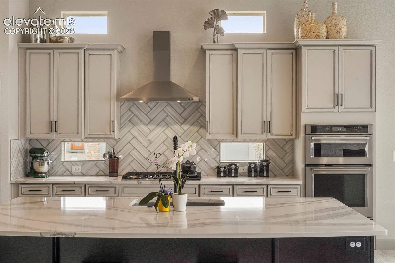Gourmet kitchen featuring a substantial island with a white countertop, light-toned cabinetry, stainless steel appliances, a herringbone tile backsplash, and a gas range