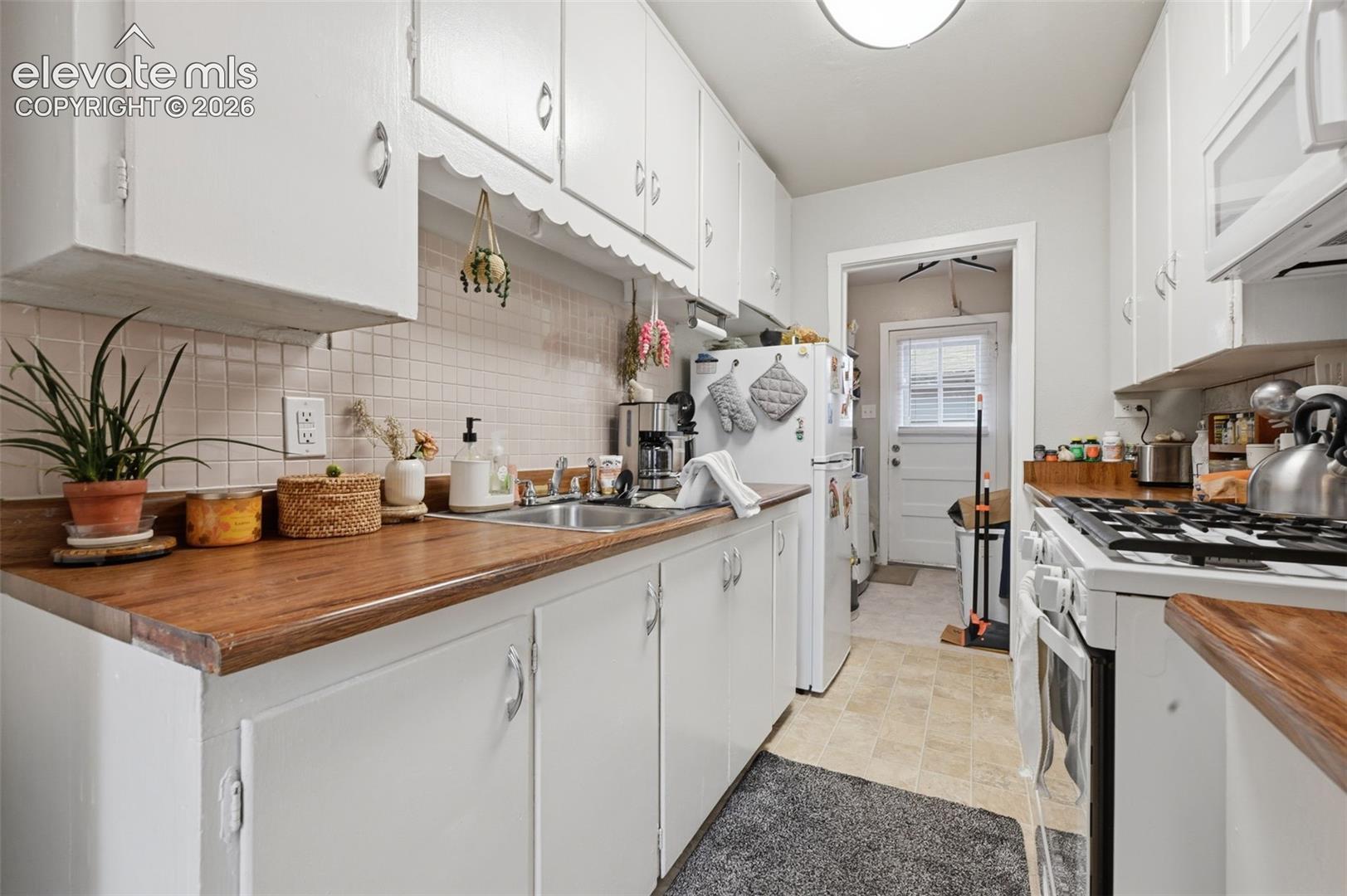 White cabinetry with scallop trim, wood-finish countertops, stainless steel sink, and a tiled backsplash
