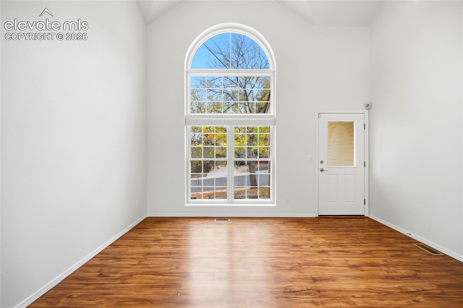Vaulted ceilings featuring an arched window, wood-finish flooring, and a glass-paneled door