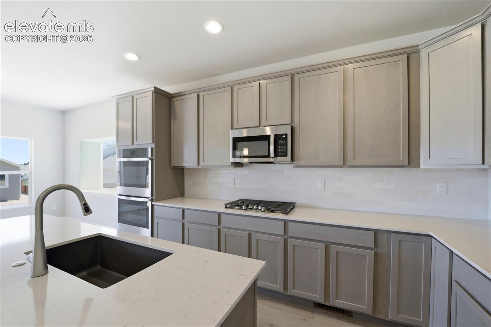 Kitchen featuring light gray shaker-style cabinetry, white quartz countertops, subway tile backsplash, stainless steel gas cooktop, and a built-in double wall oven