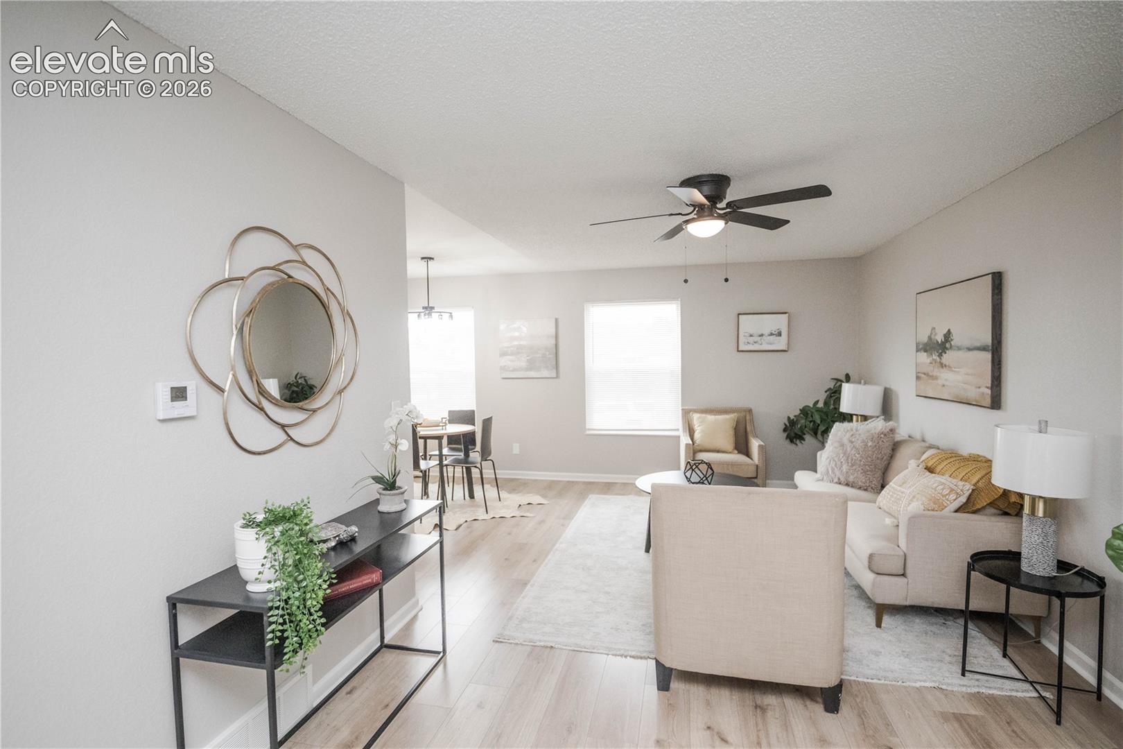 Open-concept interior featuring light wood-finish flooring, neutral-toned walls, and a ceiling-mounted light fixture with a multi-blade fan