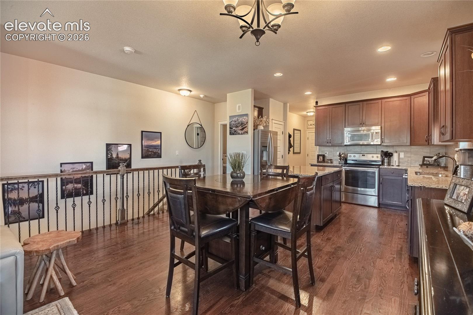 Kitchen featuring dark wood cabinetry, stainless steel appliances, stone countertops, wood-finish flooring, and metal railing accents