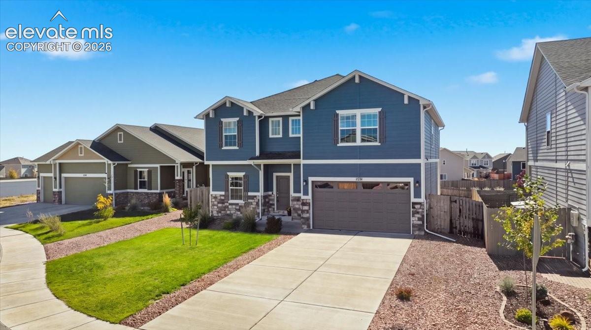 Two-story exterior featuring blue horizontal siding, stone veneer accents, an attached two-car garage, and concrete driveway
