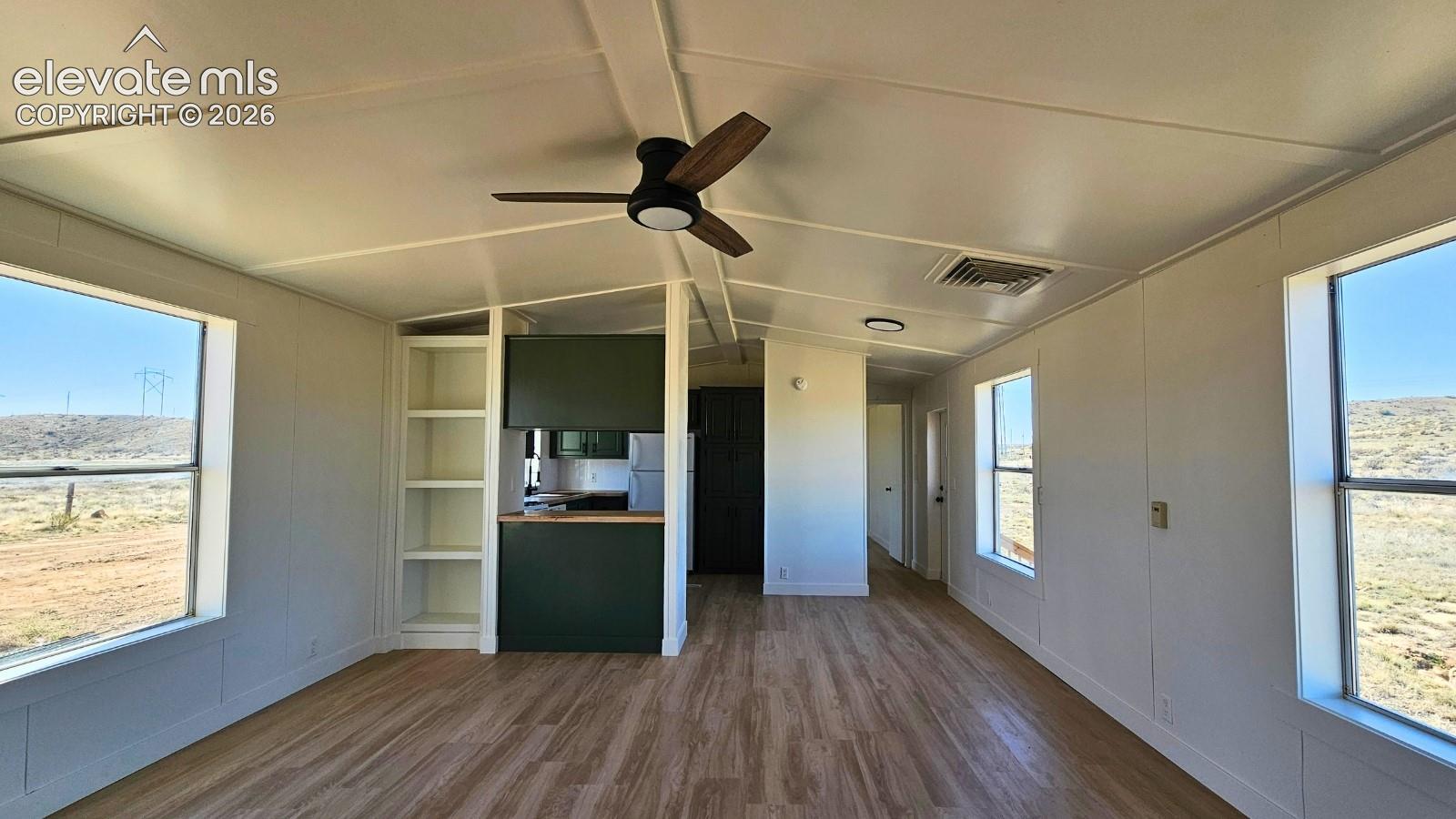 Open-concept interior with wood-finish flooring throughout, ceiling fan with dark blades, and abundant natural light from large glass doors and windows