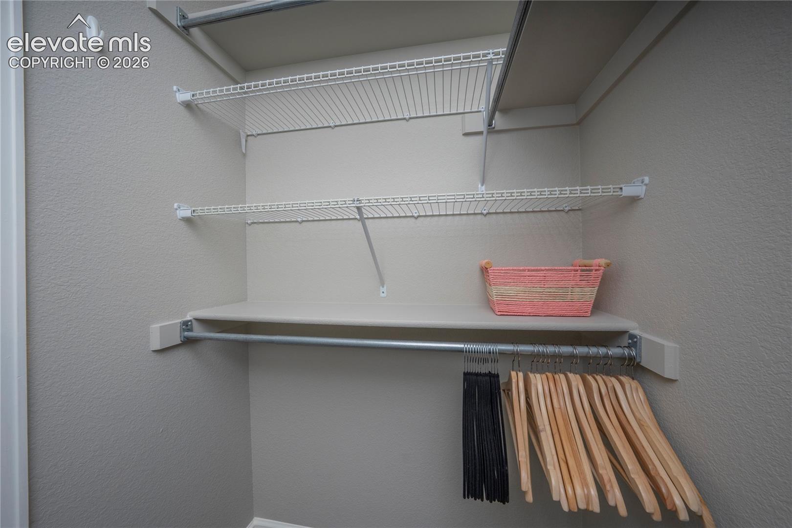 Storage area featuring adjustable wire shelving units, a solid surface shelf, and an integrated metal garment rod