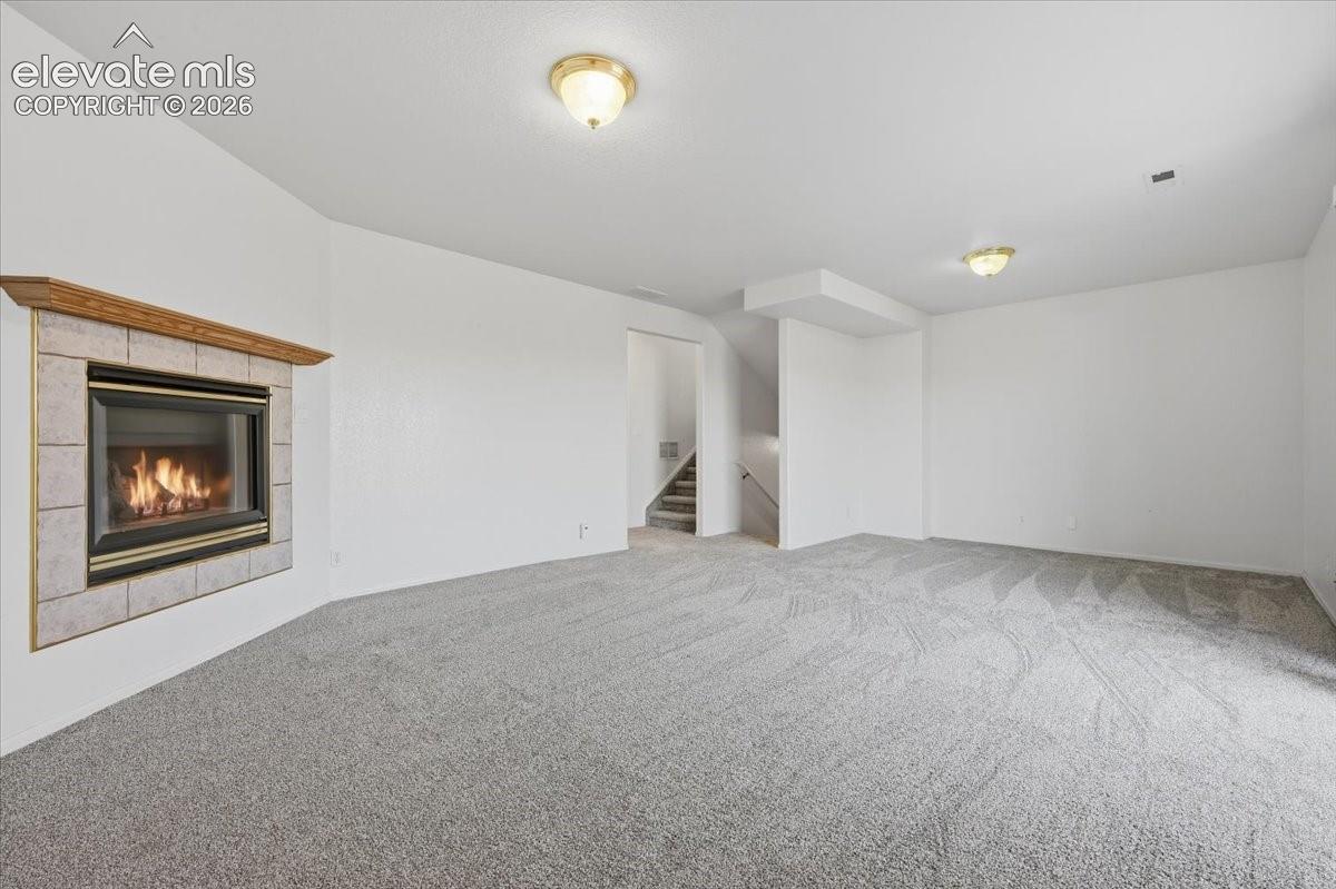 Recessed fireplace with tile surround, wood mantel, neutral carpet, and two flush-mount ceiling lights