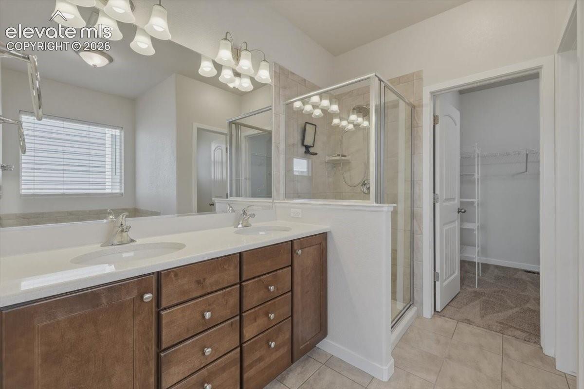 Bathroom featuring a dual vanity with wood-finish cabinetry and light countertops, a glass-enclosed shower, a built-in bathtub, and tiled flooring