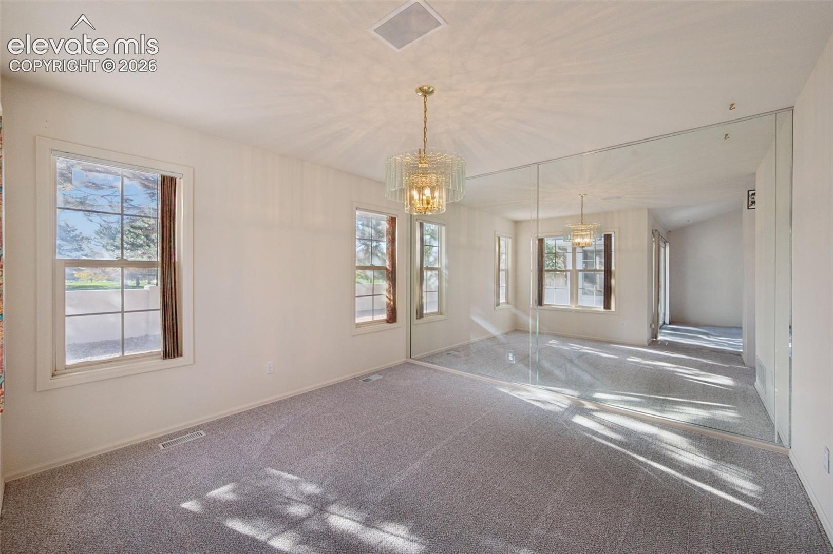 Room featuring wall-to-wall mirrored panels, multi-pane windows, carpeted flooring, and a crystal-style chandelier
